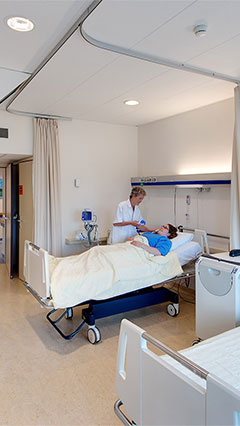 Une infirmière s'assure de l'état d'un patient dans une chambre de l'UMGC, mise en lumière par l'éclairage Philips économe en énergie