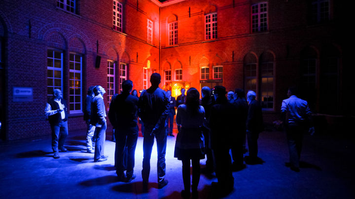 Een grote groep mensen discussieert buiten een fraai verlicht gebouw in Turnhout, België, tijdens een door Philips georganiseerde workshop