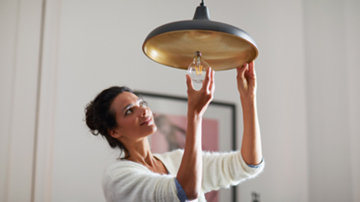Vrouw die thuis een lamp voor huishoudelijk gebruik indraait
