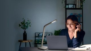 Studerende vrouw aan bureau met verstelbare LED-taaklamp, die optimale verlichting biedt voor huiswerk in kleurrijke studieruimte.