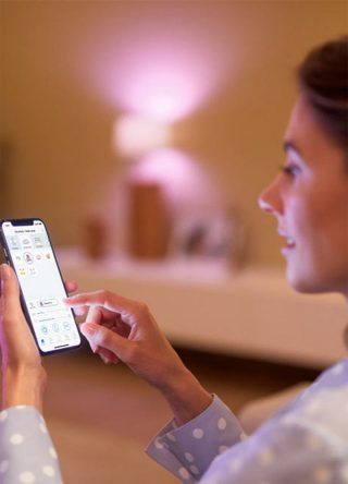 "Une femme contrôle l'éclairage LED connecté via une application pour smartphone, ajustant la lueur ambiante rose pour une atmosphère personnalisée."